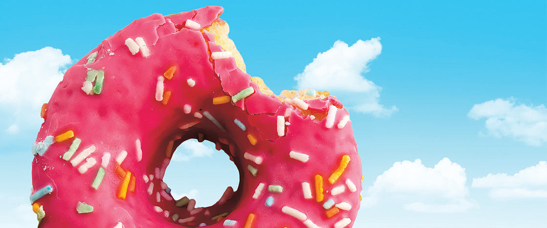 Pink frosted sprinkle doughnut with a bite taken out of it and a sky backdrop